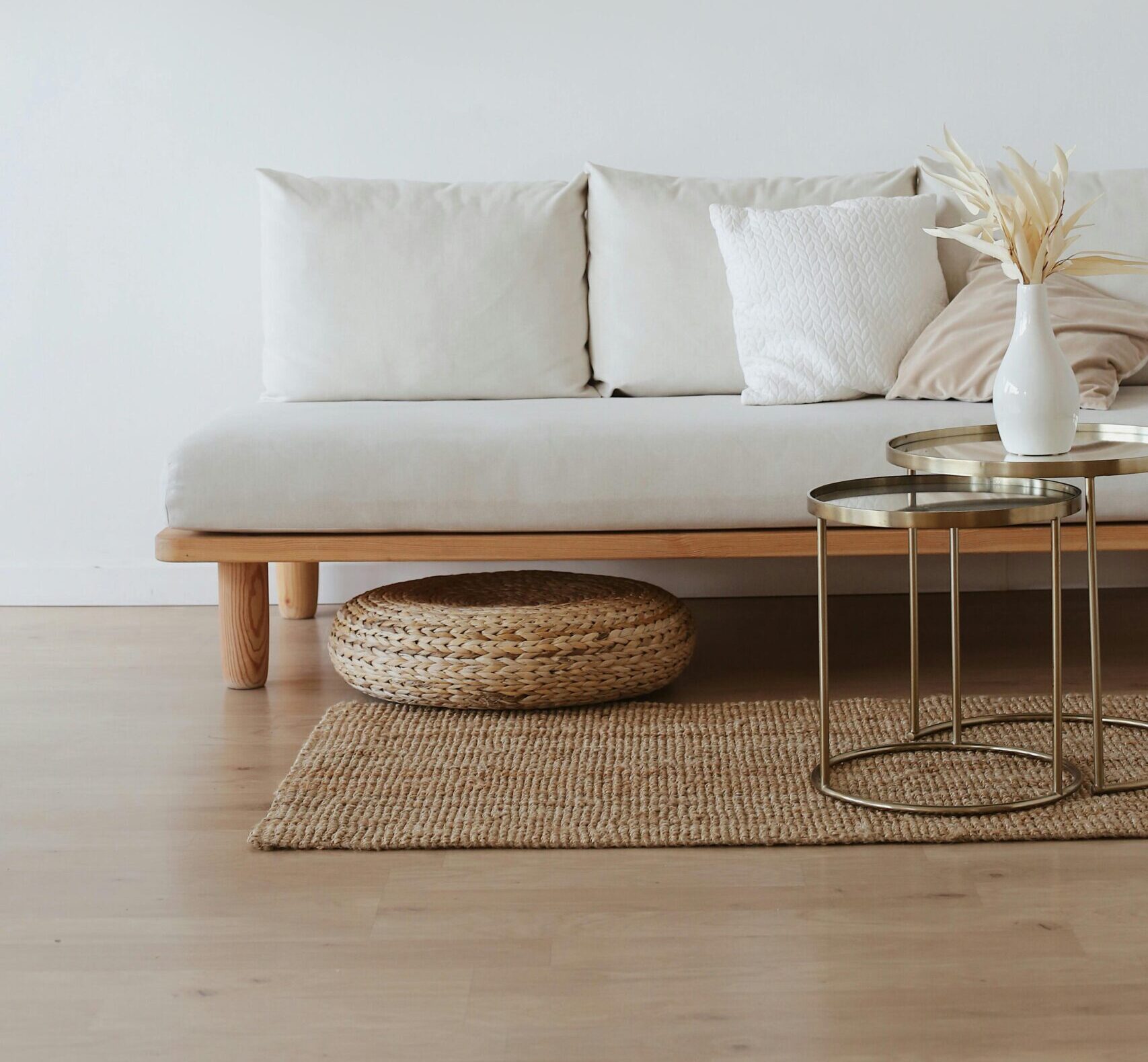 A chic minimalist living room featuring a white sofa with cushions, dried flowers in a vase, and a wooden floor.